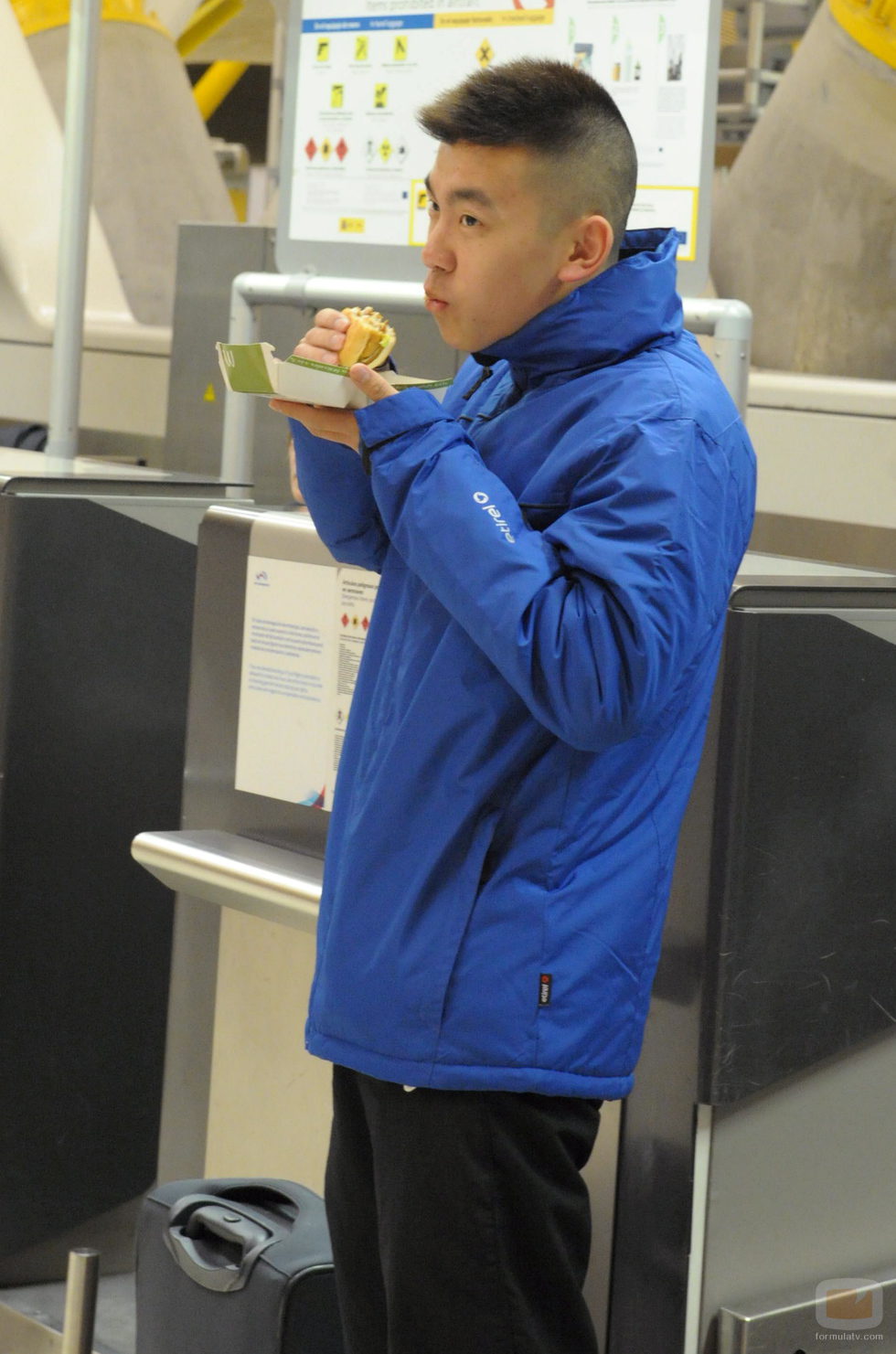 Yong Li ameniza la espera en el aeropuerto comiendo una hamburguesa