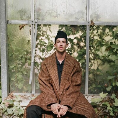 Manu Ríos, sentado en ventanal envuelto de hiedra para GQ