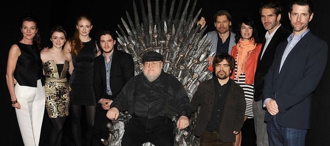 George RR Martin sentado en el trono de hierro rodeado de los actores y productores de la serie